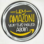 A circular novelty sign featuring a black background with white hand-drawn circle lines, yellow text reading 'Hey AMAZON! yup, THIS house Again', and a yellow smiley face inspired by the Amazon logo.