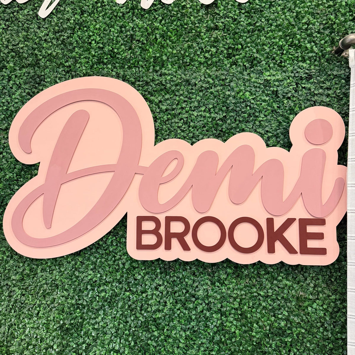 Layered first and middle name sign displayed on a greenery wall as a baby shower backdrop