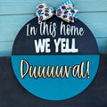 A 3D door hanger with a blue and black color scheme. It has the text 'In this HOME we YELL DUUUUUVAL!!' in bold letters, and a decorative bow at the top.
