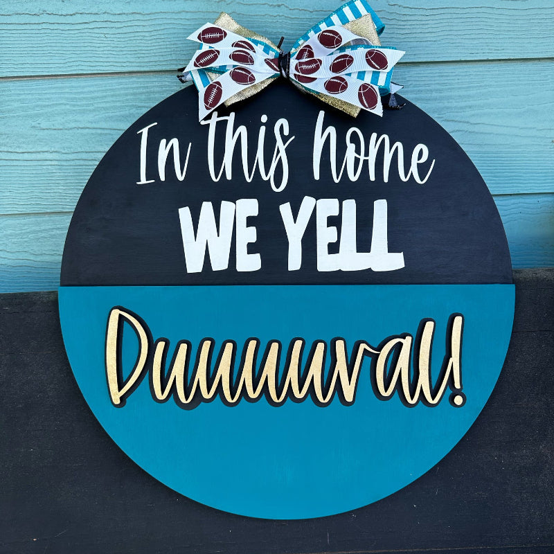 A 3D door hanger with a blue and black color scheme. It has the text 'In this HOME we YELL DUUUUUVAL!!' in bold letters, and a decorative bow at the top.