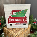 A vintage-style lighted sign featuring a red and white truck with a decorated Christmas tree on top, surrounded by festive decorations.