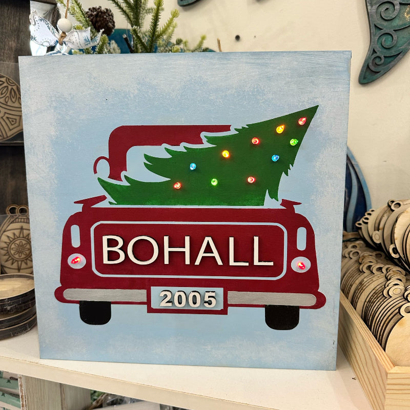 Decorative sign with a red truck carrying a Christmas tree, featuring the name 'BOHALL' and the year '2005'.