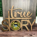 A wooden nativity display with multiple layers, featuring the text 'True Story' on the top layer, and a circular depiction of the nativity scene.