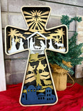 A layered cross decoration featuring a geometric pattern with gold, black, and white colors, with a backdrop of a Christmas tree and presents.