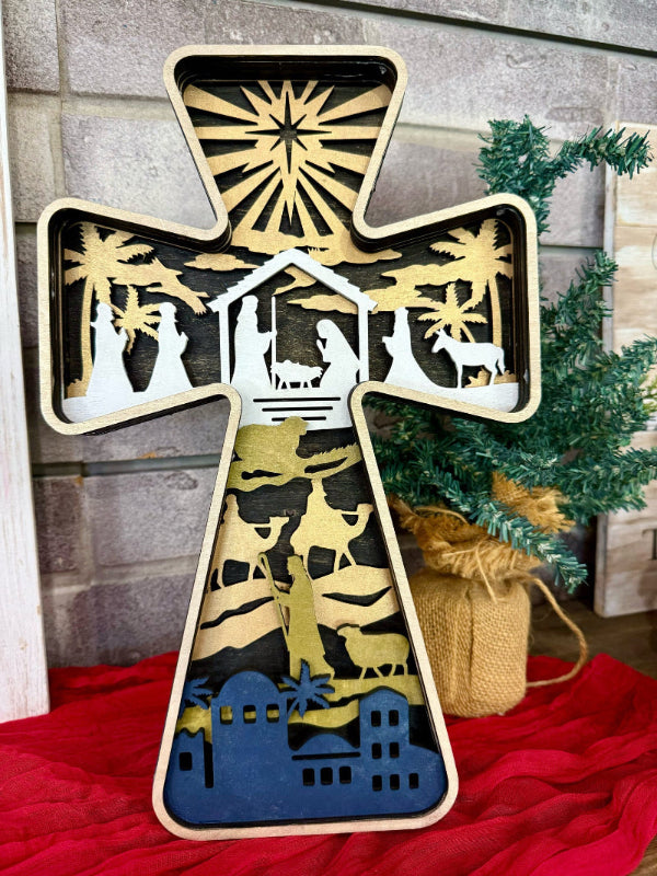 A layered cross decoration featuring a geometric pattern with gold, black, and white colors, with a backdrop of a Christmas tree and presents.