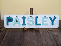 A customized wooden name puzzle with the name 'Paisley' written in blue.