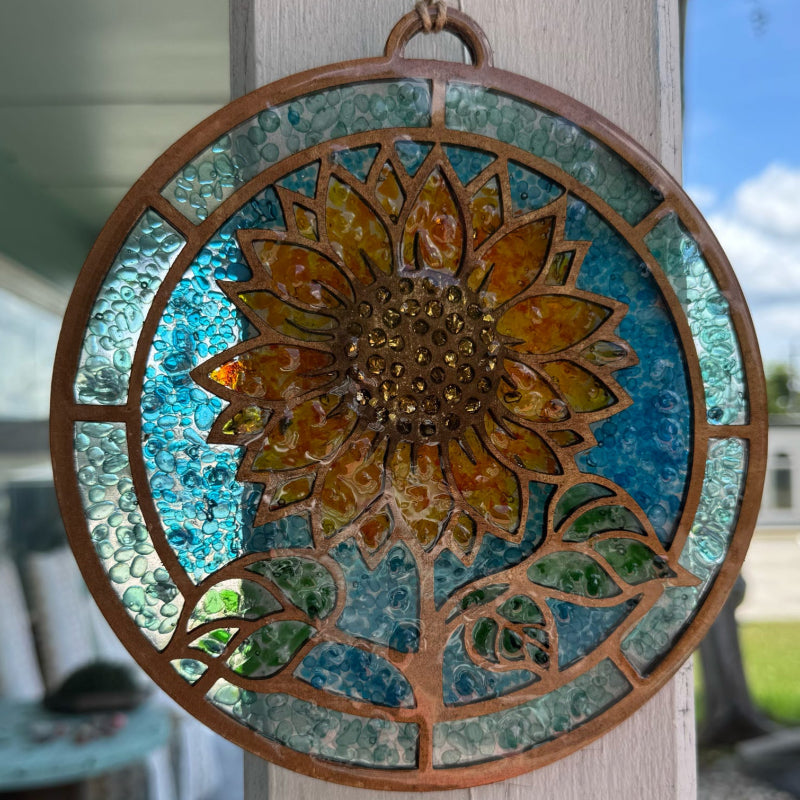 Decorative sunflower mosaic hanging on a wooden post with a blurred outdoor background