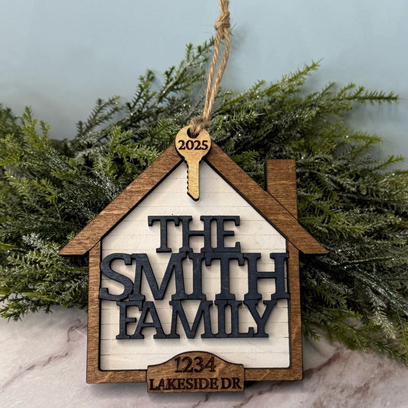 Wooden house-shaped ornament with 'The Smith Family' and address on a marble surface with greenery.