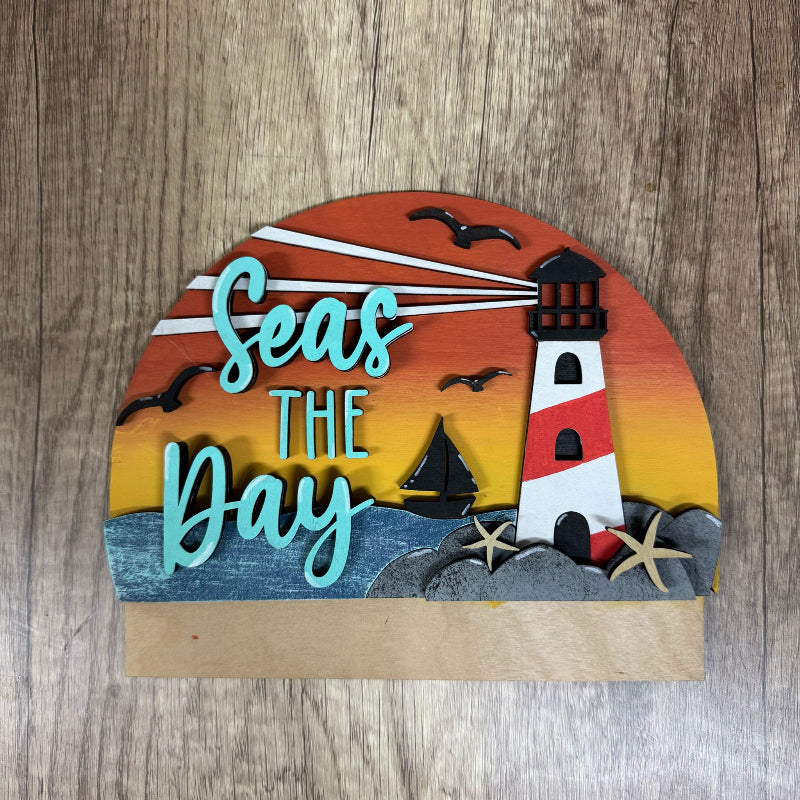 Decorative sign with lighthouse and 'Seas The Day' text on a wooden background