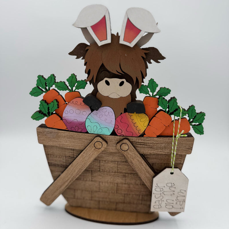 Cardboard cutout of a character with bunny ears in a basket with carrots and Easter eggs on a white background.