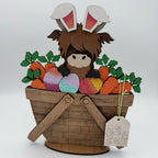 Cardboard cutout of a character with bunny ears in a basket with carrots and Easter eggs on a white background.