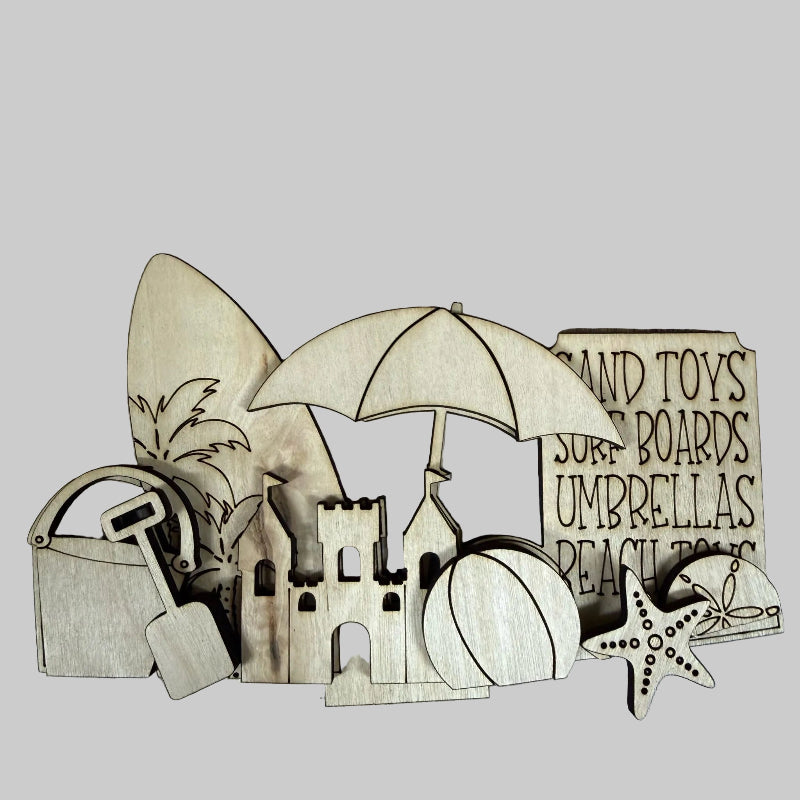 Wooden beach-themed cutouts including a sandcastle, umbrella, surfboard, and toys on a wooden surface.
