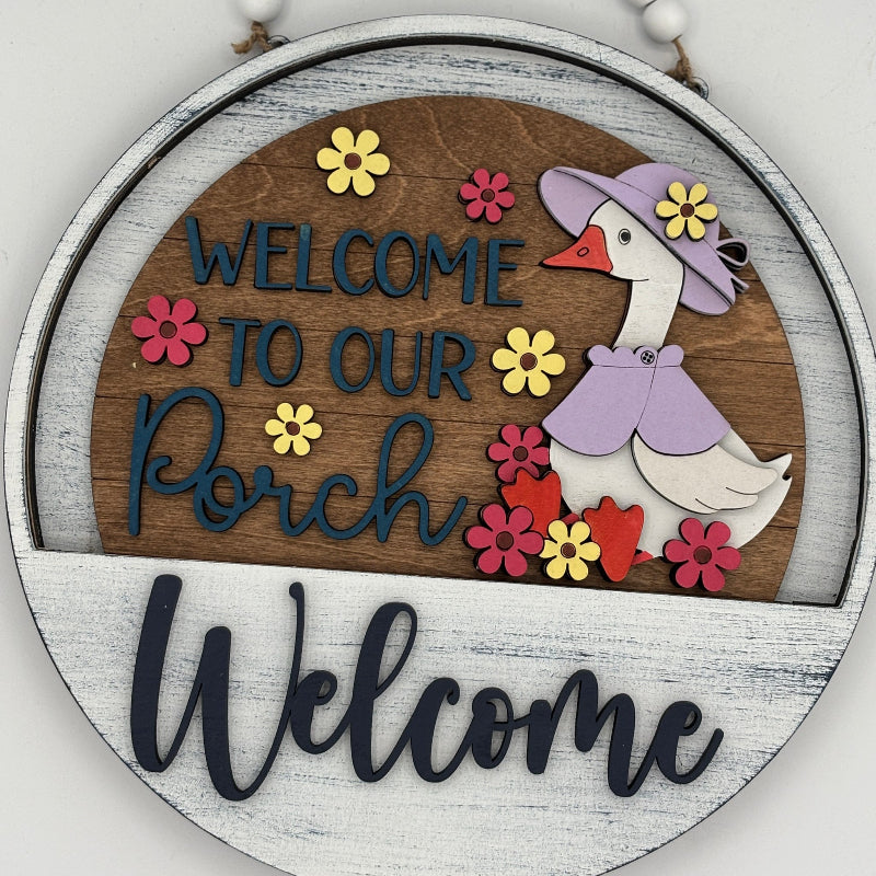 Decorative sign with a goose illustration and 'Welcome to our Porch' text on a wooden background.