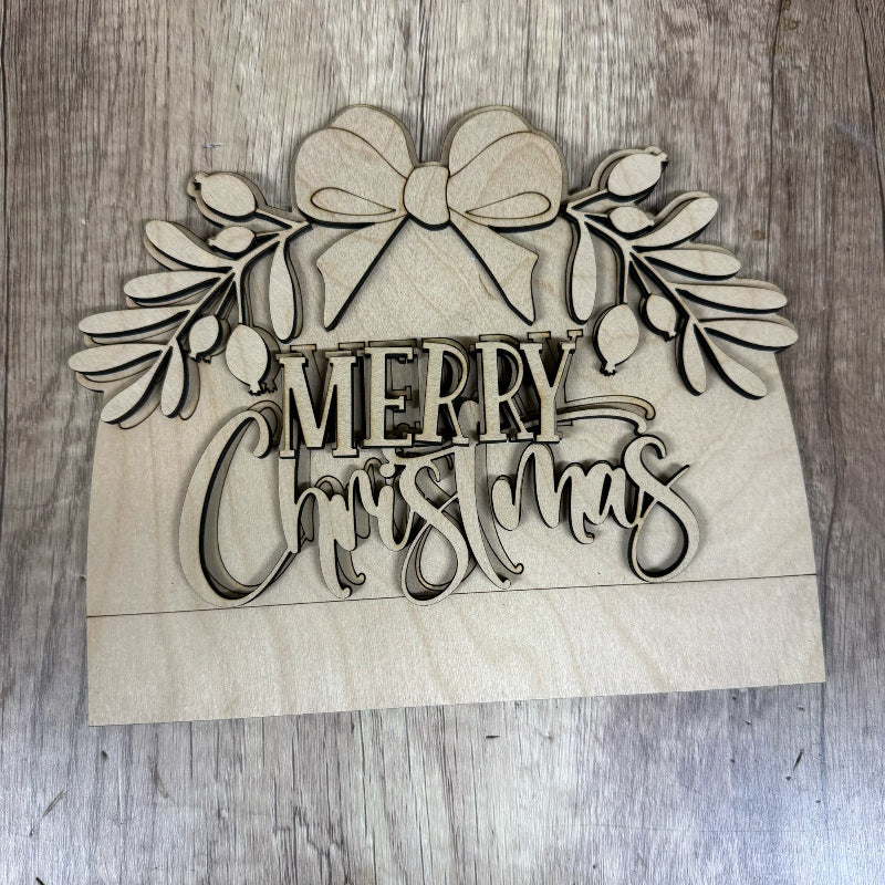 Wooden 'Merry Christmas' decoration with a bow and foliage on a wooden surface