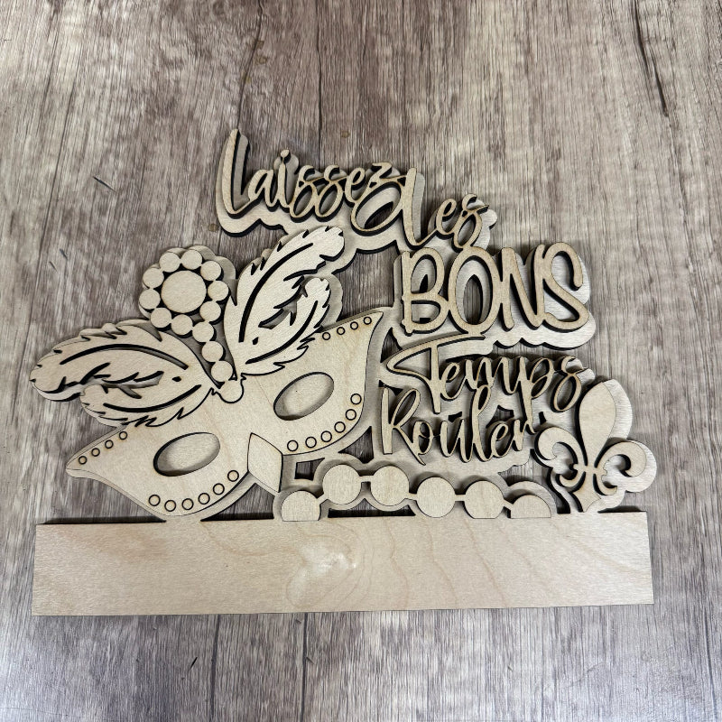 Wooden decorative item with a mask design and French text on a wooden surface