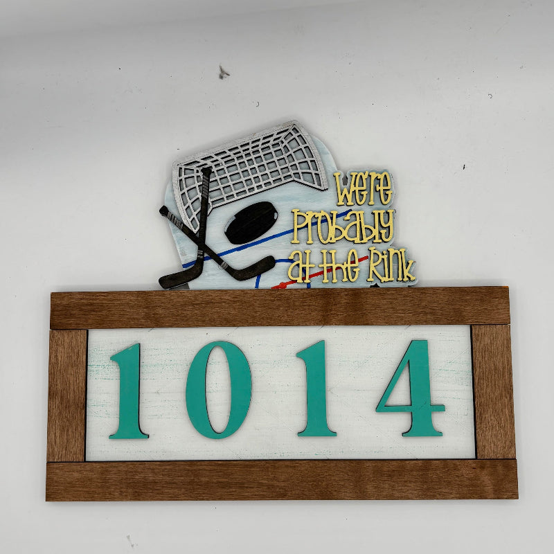 Decorative sign with hockey helmet, stick, and text 'We're Probably at the Rink' on a white background.
