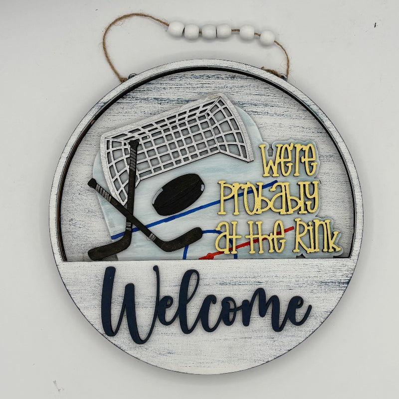 Decorative sign with hockey-themed design and text 'We're probably at the rink. Welcome' on a white background.