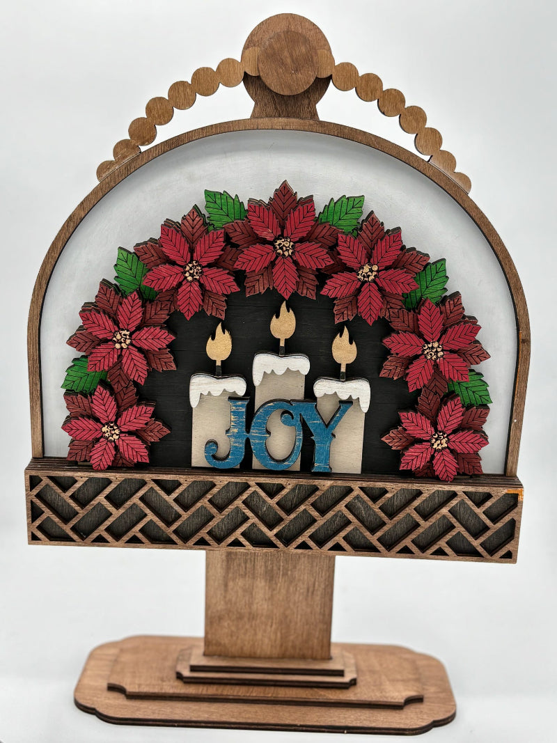 Decorative wooden sign with poinsettias and candles spelling 'JOY' on a white background