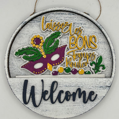 Decorative round sign with Mardi Gras-themed design and 'Welcome' text on a white background.