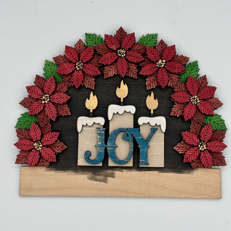 Decorative wall art with poinsettias, candles, and 'JOY' letters on a white background