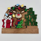 Decorative sign with a reindeer, gift, and Christmas tree, featuring festive text on a white background.