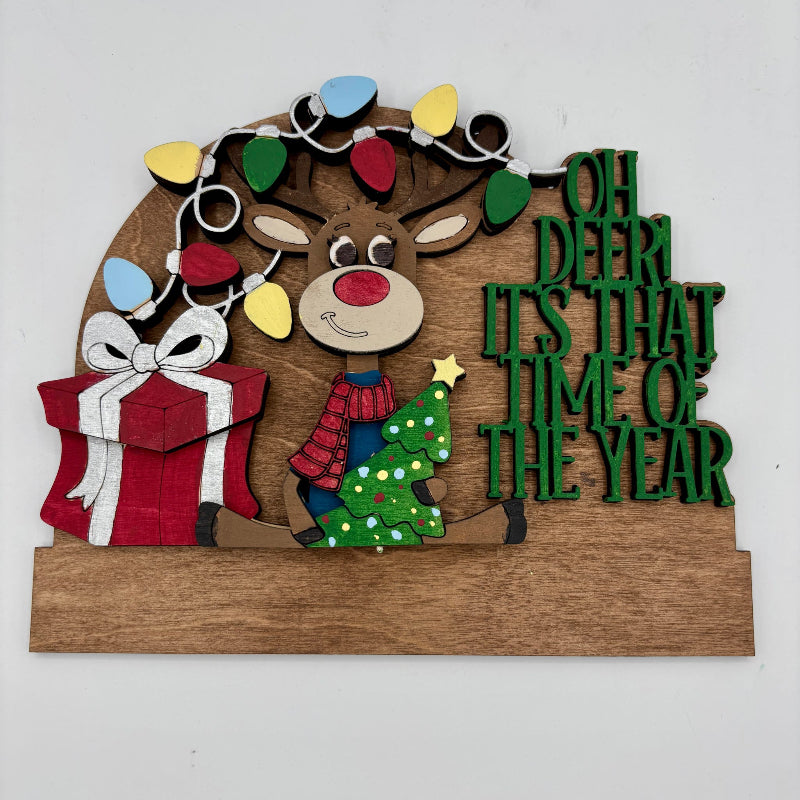 Decorative sign with a reindeer, gift, and Christmas tree, featuring festive text on a white background.