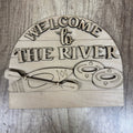 Wooden sign with 'Welcome to the River' text and kayak design on a wooden background