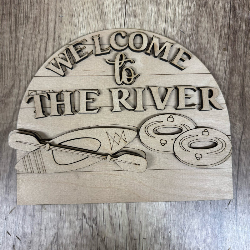 Wooden sign with 'Welcome to the River' text and kayak design on a wooden background