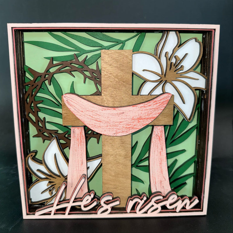 Decorative cross with floral elements and 'He is risen' text on a green background