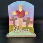 Decorative cross with heart and 'Risen' text on a colorful background