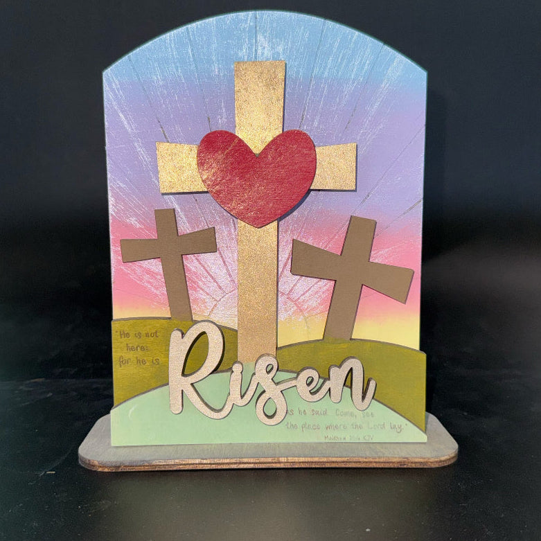 Decorative cross with heart and 'Risen' text on a colorful background