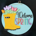 Decorative sign with a yellow rain boot, flowers, and 'Welcome Spring' text on a black background.