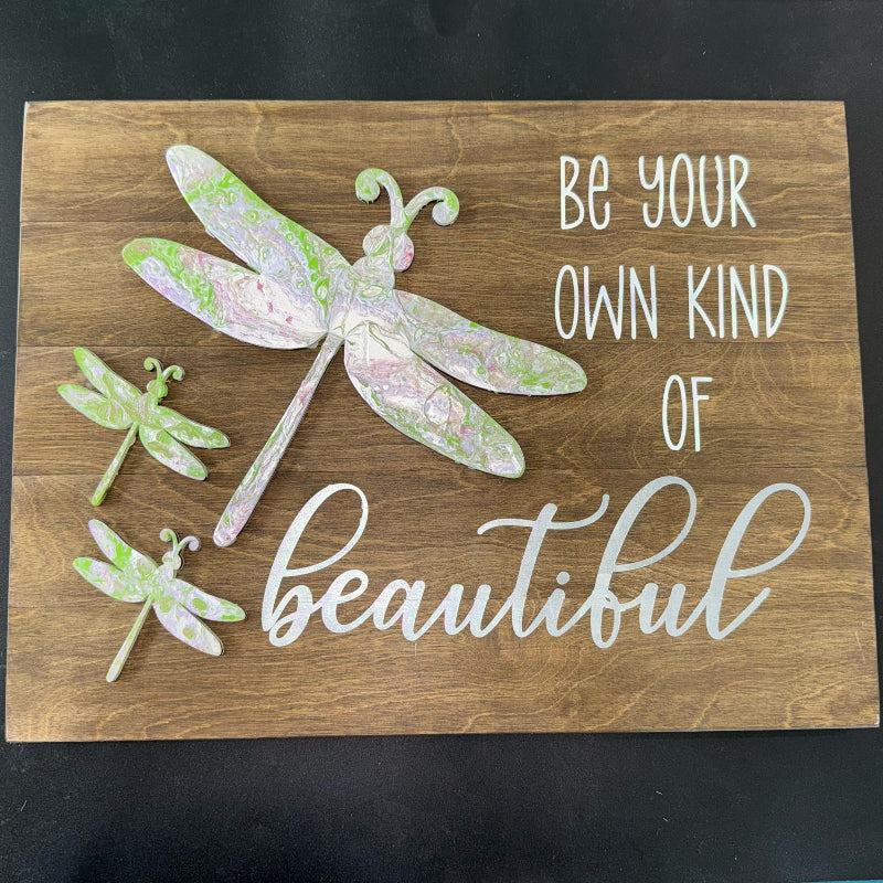 Wooden sign with dragonfly designs and motivational text on a dark background