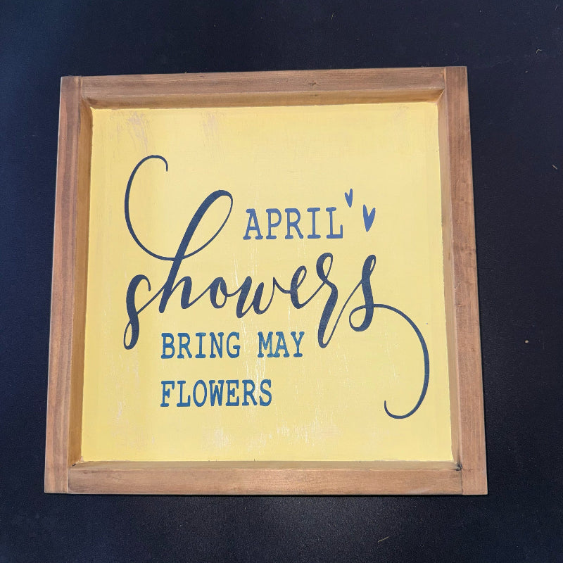 Wooden-framed sign with 'April Showers Bring May Flowers' text on a yellow background