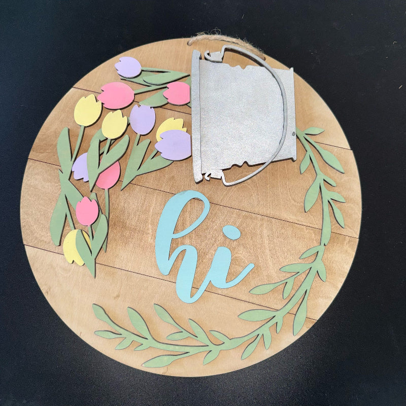 Decorative wooden round sign with floral design and 'hi' text on a black background