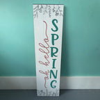 Wooden sign with 'Spring Hello' text against a teal wall