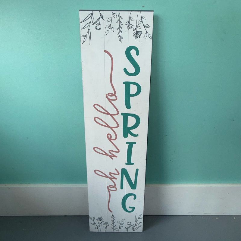 Wooden sign with 'Spring Hello' text against a teal wall