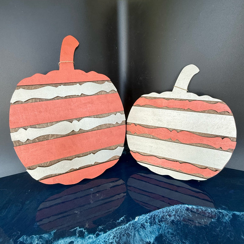 Two paper pumpkin decorations with striped pattern on a reflective surface.