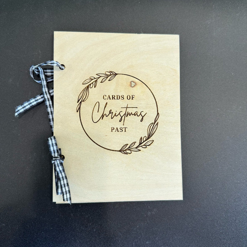 Wooden card with 'Cards of Christmas Past' text and a plaid ribbon on a dark background