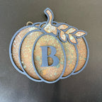 Decorative pumpkin-shaped ornament with letter 'B' on a dark background