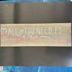 Wooden plaque with 'All you need is love' text on a dark surface