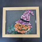 Decorative pebble art of a witch's hat and pumpkin in a wooden frame on a dark background