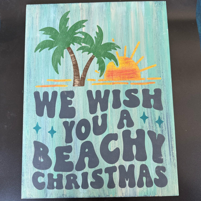 Wooden sign with 'We wish you a beachy Christmas' text and palm tree design on a teal background.