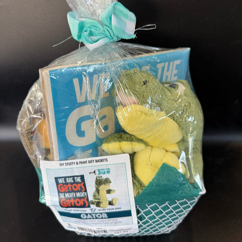 Gift basket with plush gators and a card, wrapped in clear cellophane with a blue ribbon on a dark background.