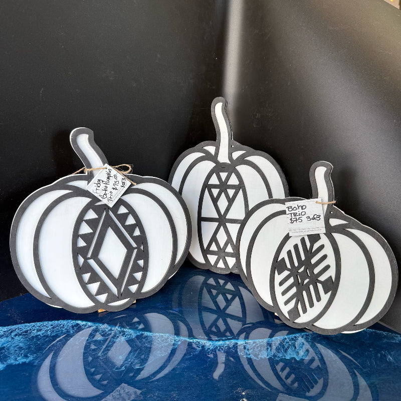Three white pumpkin-shaped cutting boards with black patterns on a blue surface.