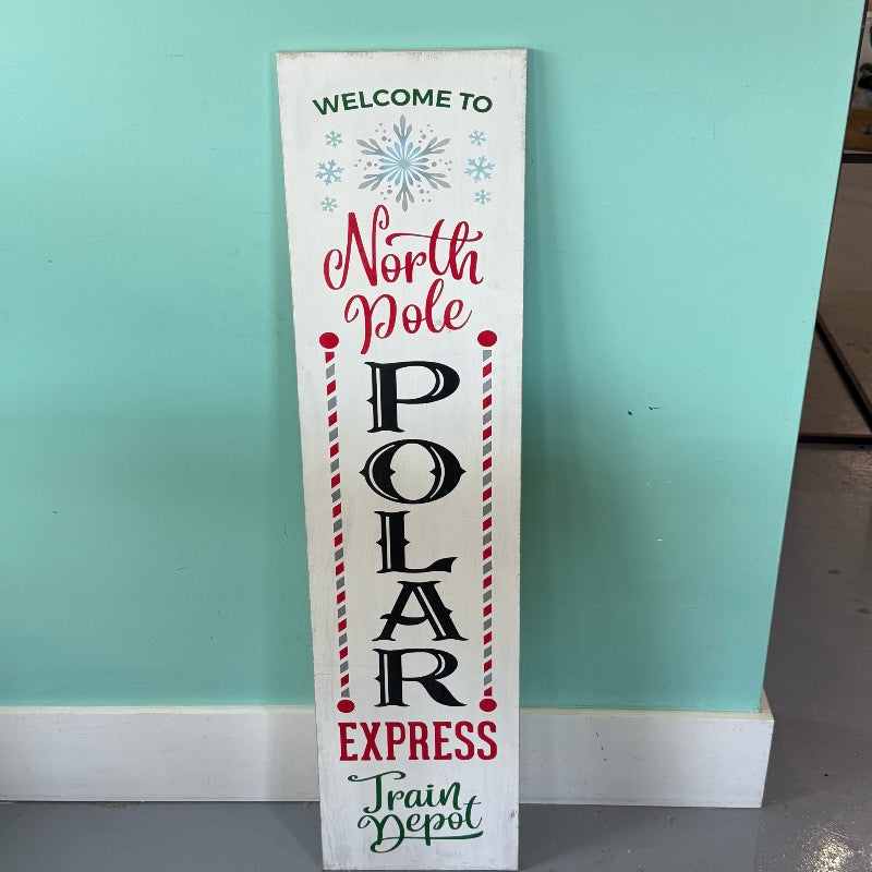 Christmas-themed sign with text 'Welcome to North Pole Polar Express Train Depot' against a teal wall.