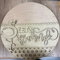 Wooden round sign with 'Let's Flamingle' text and flamingo design on a wooden surface.