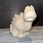 Unpainted ceramic dinosaur figurine on a wooden surface with a dark background