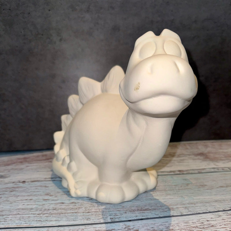 Unpainted ceramic dinosaur figurine on a wooden surface with a dark background