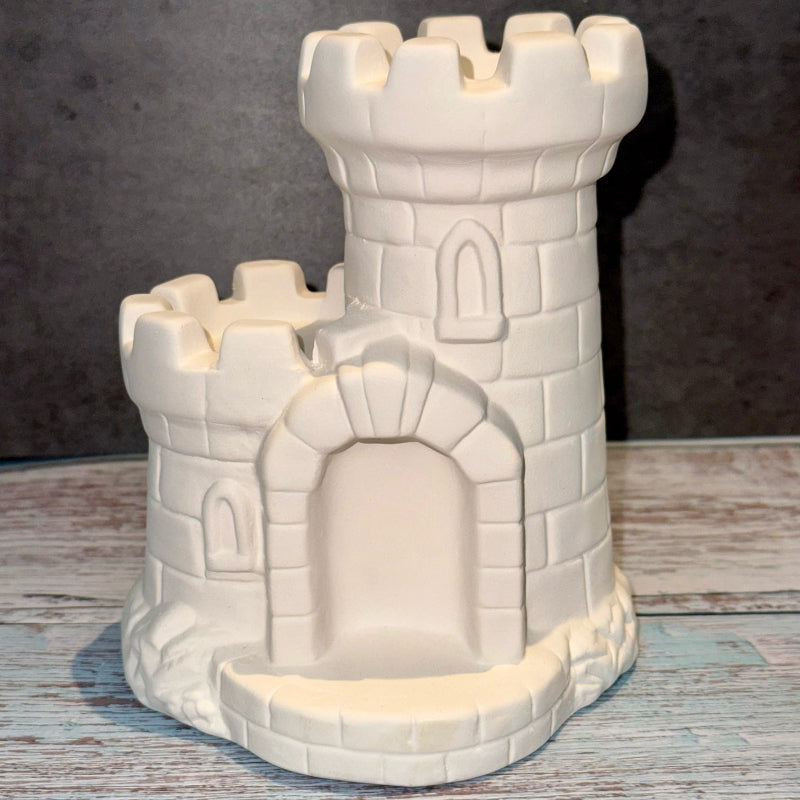 White ceramic castle-shaped candle holder on a wooden surface with a dark background